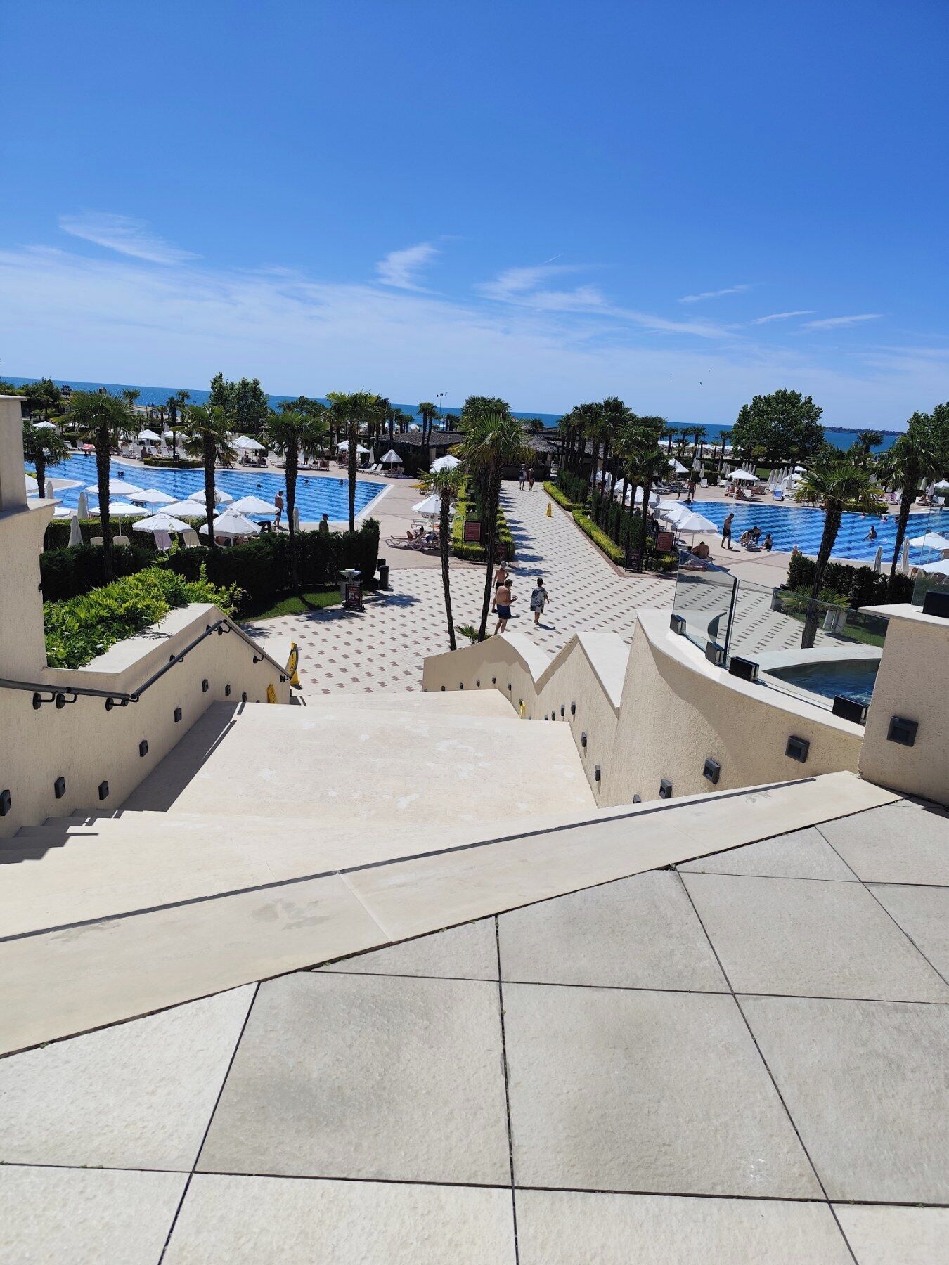 A resort pool area with multiple swimming pools, palm trees, and a clear view of the ocean.