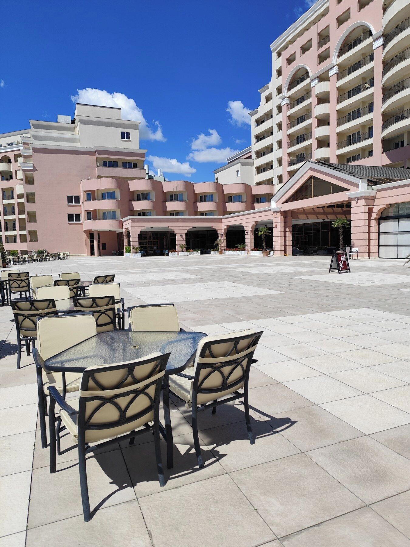 A hotel courtyard with outdoor seating, a large entrance, and a multi-story building with balconies.