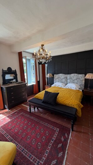 Um quarto com uma cama, um banco, uma cômoda, um candelabro e um tapete estampado.