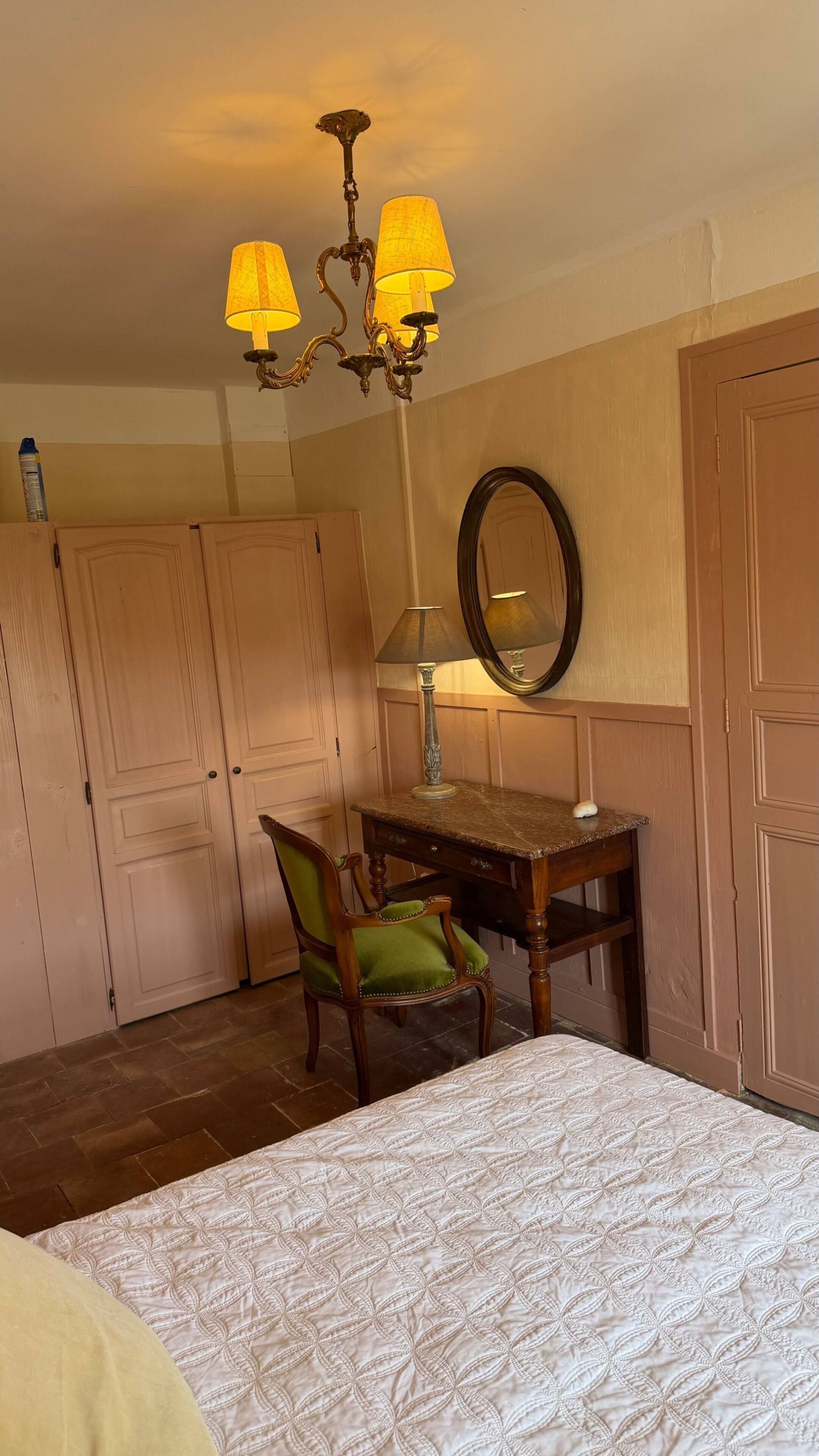 Une chambre à coucher avec un lit, un bureau avec une chaise, un miroir et un lustre.
