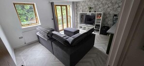 Un salón moderno con sofá, mueble para televisión y vistas a zonas verdes.
