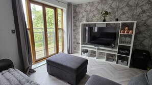 A living room with a TV, grey sofas, a herringbone floor, a balcony with a view, and a snack bar. - Pet Friendly 2-bed Apt, Sleeps 3 With Parking (Doncaster)