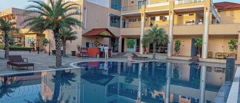Un hotel de varios pisos con piscina, palmeras y cielo despejado.