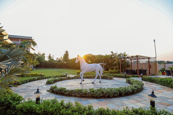 A white horse statue in a circular stone plaza with surrounding greenery and a building in the background. - Gautam Hotel Dhanusha  (Mithila)