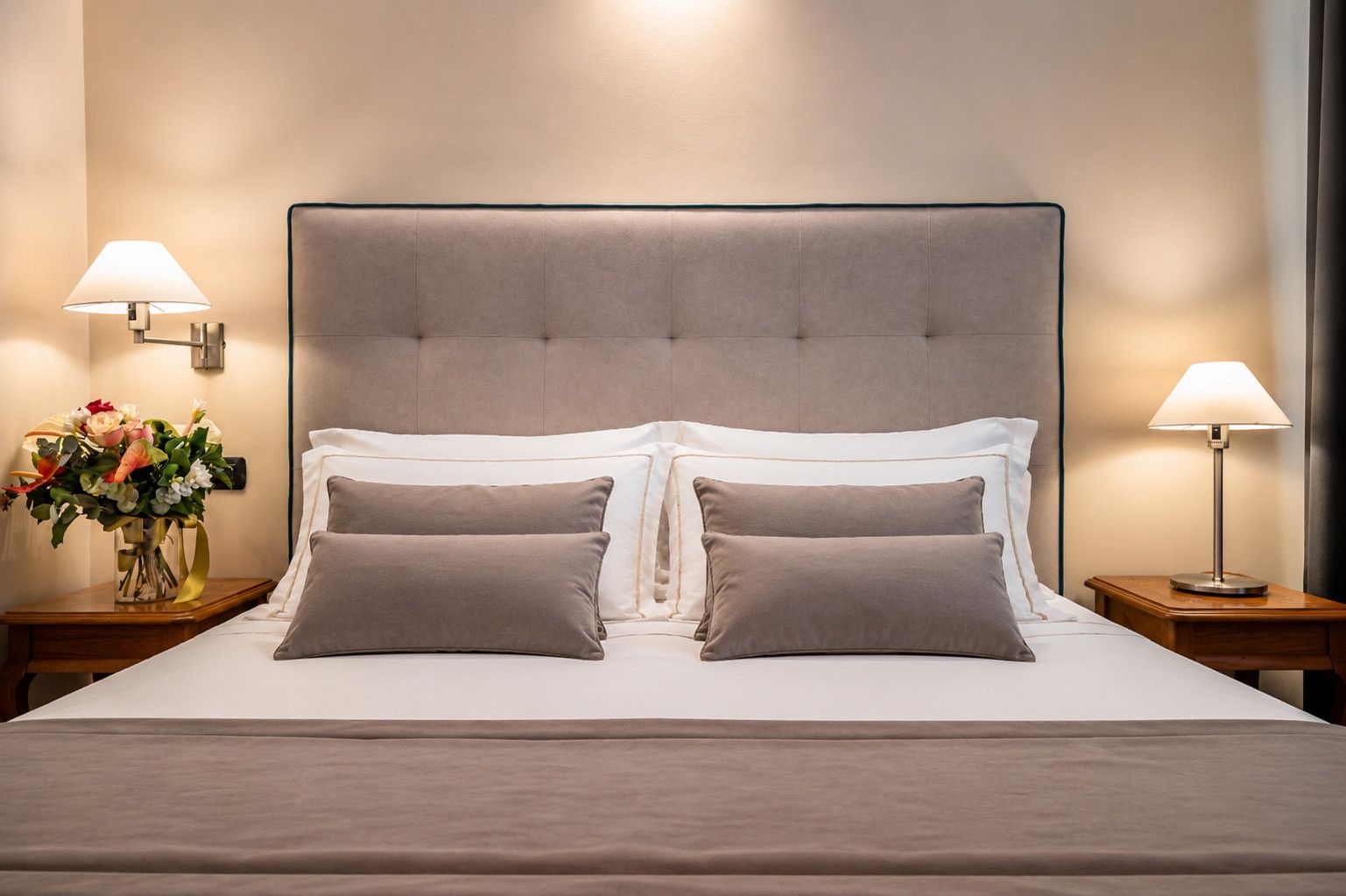 A neatly made bed with a tufted headboard, two bedside tables with lamps, and a vase of flowers on one table.