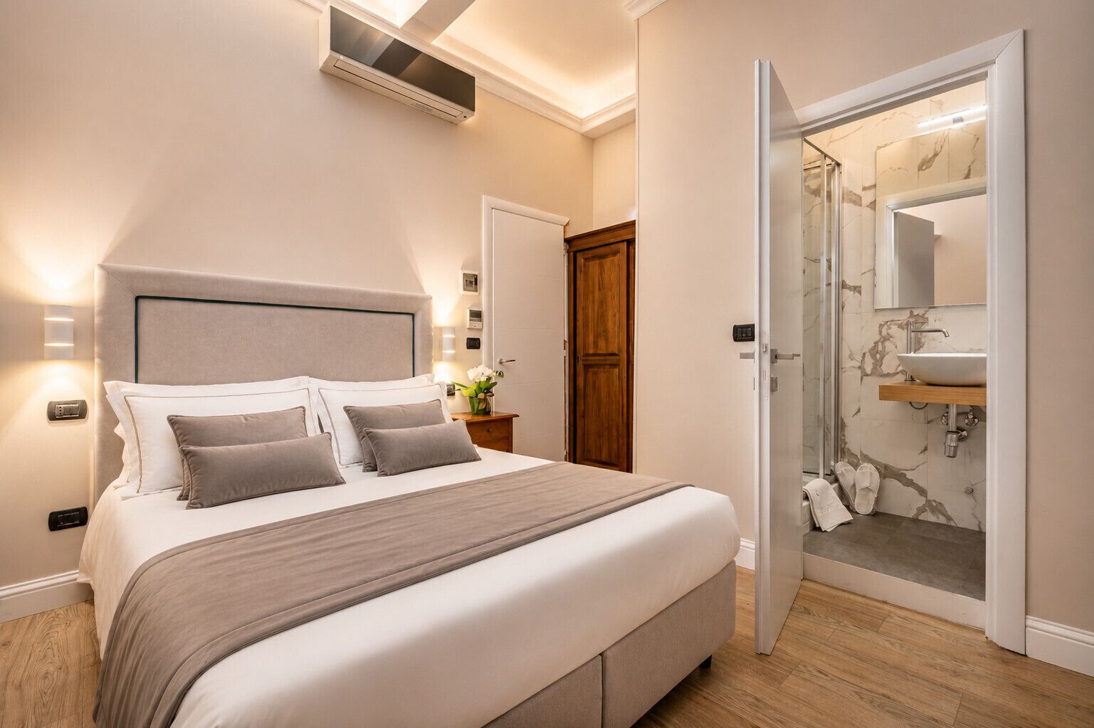 A bedroom with a bed, bedside tables, a wardrobe, and a bathroom with a sink and mirror.