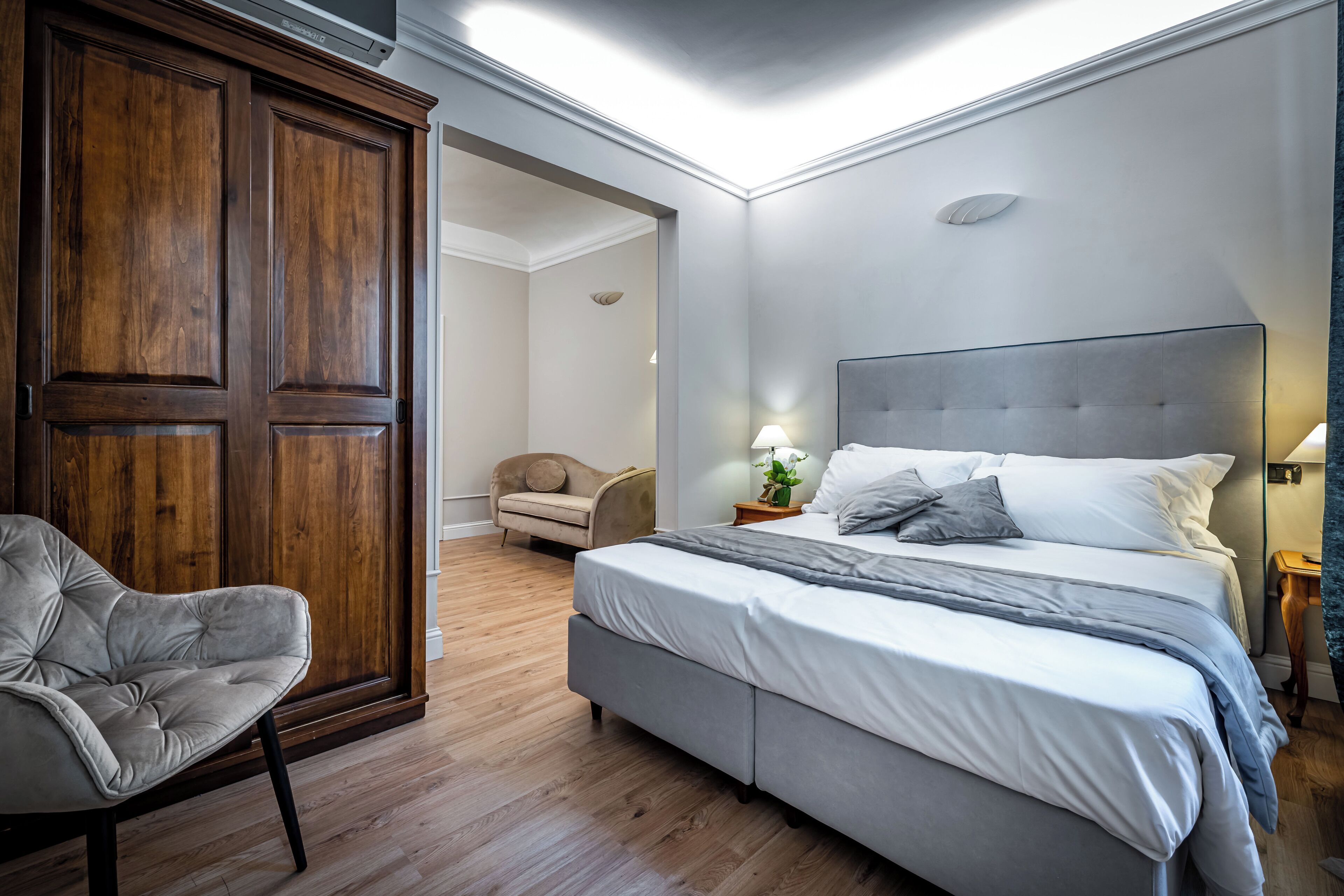 A bedroom with a large bed, a chair, a wardrobe, and a door leading to another room.