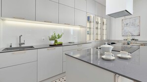 Eine moderne Küche mit weißen Schränken, einer Edelstahl-Arbeitsplatte und einer zentralen Kochinsel mit zwei weißen Tassen und Untertellern.