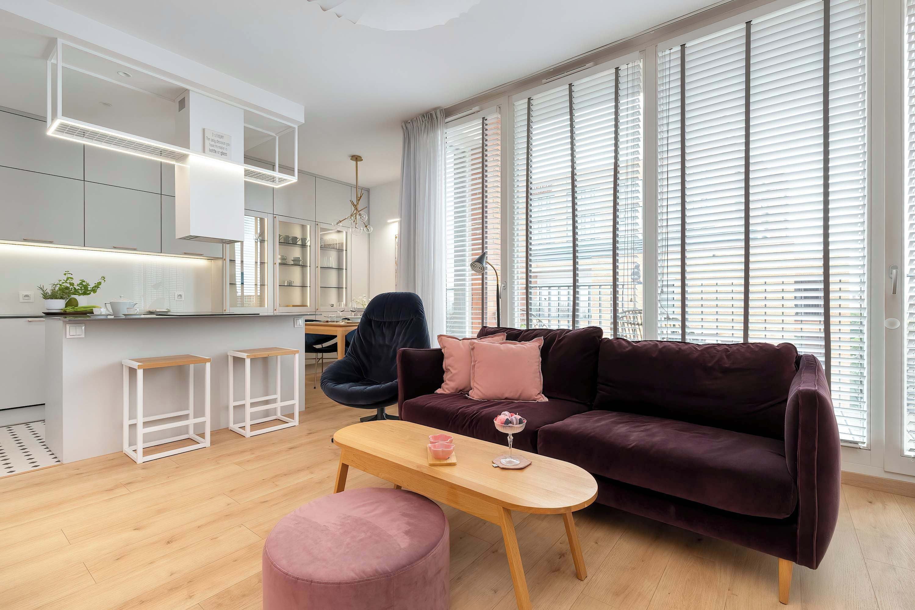 A modern living room with a dark purple sofa, a wooden coffee table, and a pink ottoman.
