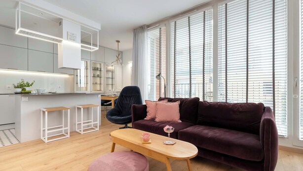 Ein modernes Wohnzimmer mit einem dunkelvioletten Sofa, einem Holztisch und einem pinkfarbenen Hocker.