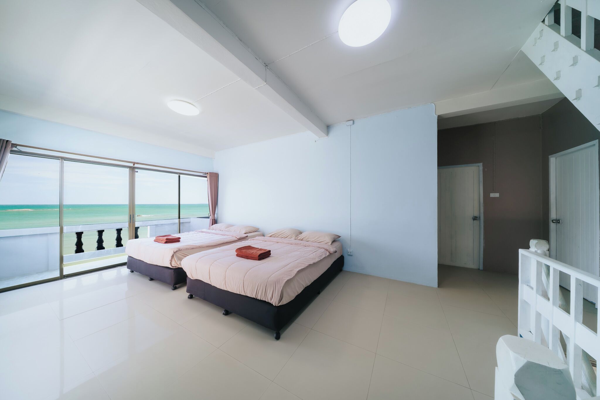 A bedroom with two beds, a balcony with a view, and a staircase.