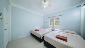 A room with two beds, a ceiling fan, a window with curtains, and a door.