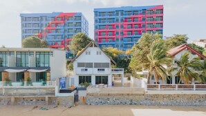 A beachfront property with a pool, a white building with a balcony, and colorful buildings in the background. - GAO Bee One Beachfront Pool Villa (Ban Chang)