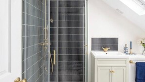 Une salle de bain moderne avec une douche à parois de verre, un meuble-lavabo blanc doté de poignées dorées et une serviette bleue.