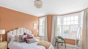 Une chambre à coucher avec un grand lit, une table de chevet, une chaise et une fenêtre avec des rideaux.