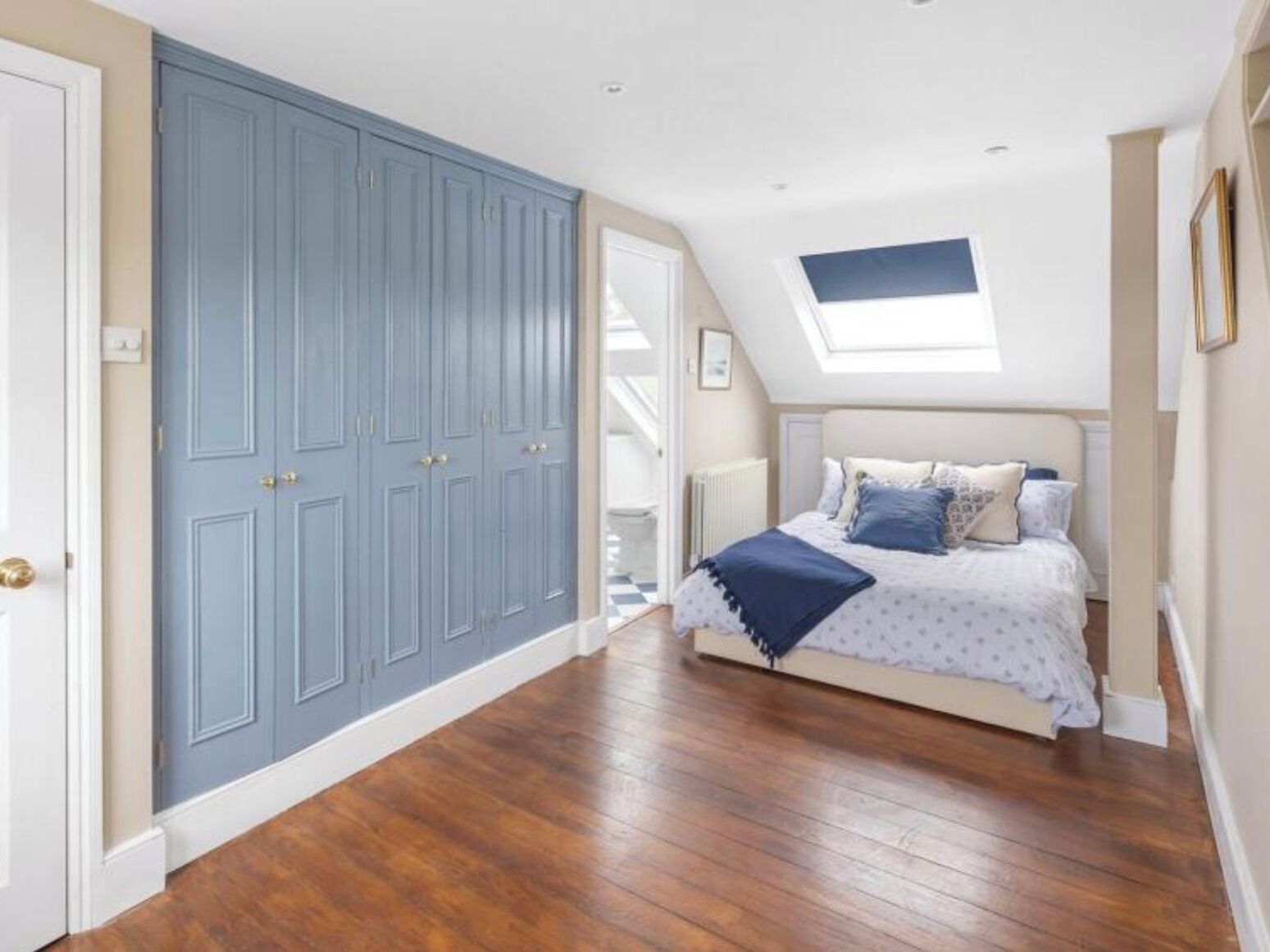 Quarto com um guarda-roupa grande, uma cama com cobertor azul e um claraboia.
