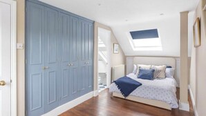 Ein Schlafzimmer mit großem Kleiderschrank, einem Bett mit blauer Decke und einem Oberlicht.