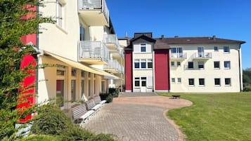 Un edificio de varios pisos con una entrada central, asientos al aire libre y un patio empedrado.
