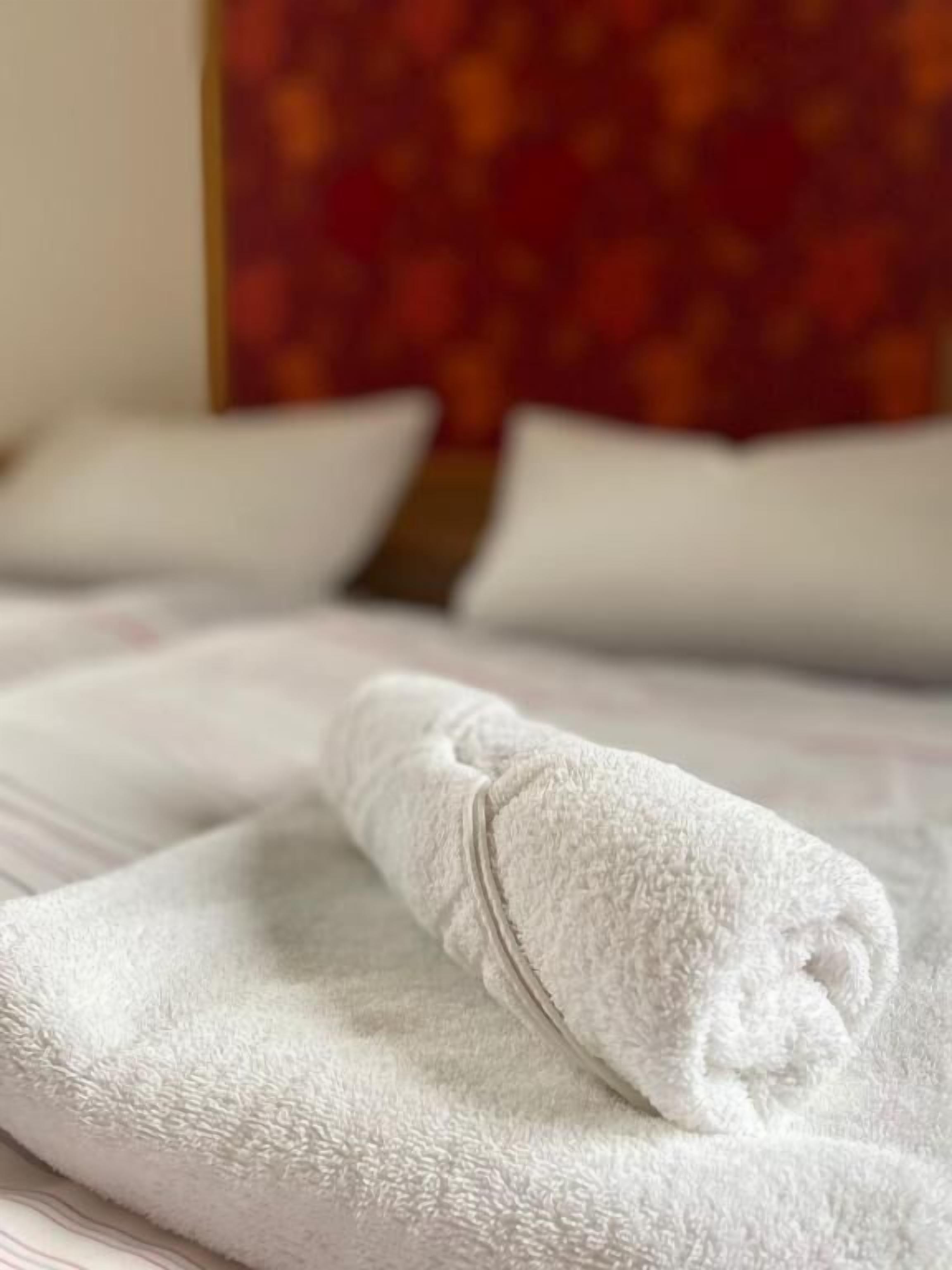 Een keurig opgemaakt witte handdoek op een bed met een gestreept hoofdeinde.
