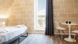 Ein Zimmer mit einem Bett, einem Vorhangfenster, einem runden Tisch mit Stühlen und Blick ins Freie.