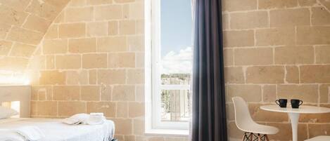 Una habitación con cama, ventana con cortinas, una mesa redonda con sillas y vista al exterior.