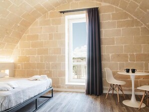 Une pièce avec un lit, une fenêtre avec des rideaux, une table ronde avec des chaises et une vue sur l’extérieur.