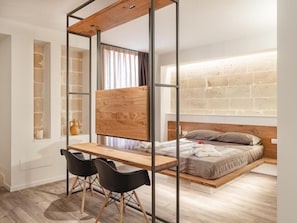 Une chambre avec un lit, un bureau, deux chaises, une fenêtre et un mur en briques.