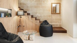 Ein modernes Wohnzimmer mit Steinwand, Holztreppe, einem schwarzen Sitzsack und einem Glastisch.