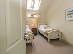 A bedroom with two single beds, a nightstand, a window with curtains, and a framed picture on the wall.