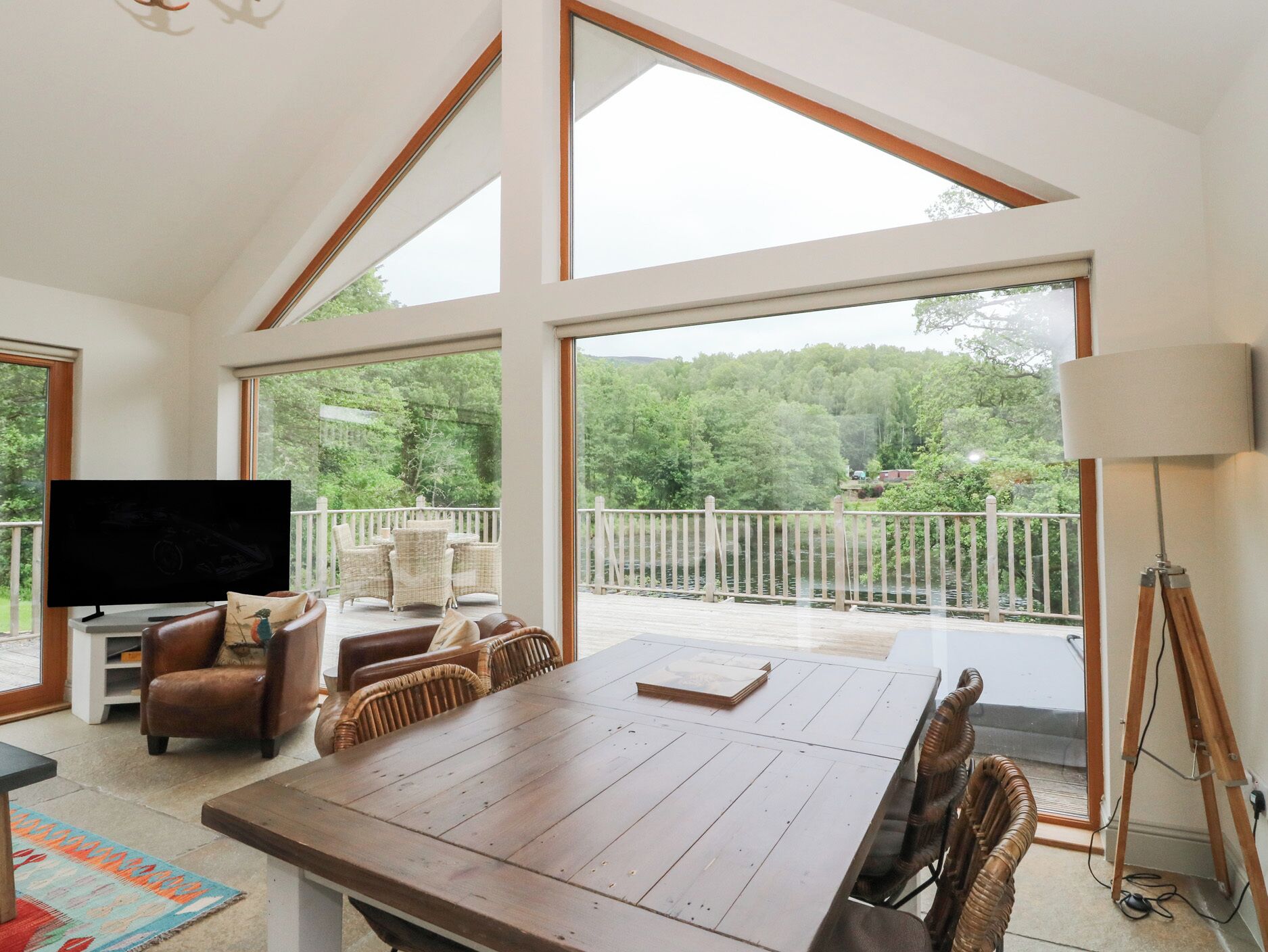 A spacious room with a large wooden dining table, wicker chairs, a television, and a balcony with a white railing.
