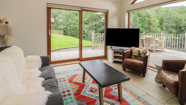 Ett vardagsrum med en soffa, ett soffbord och en tv som står på ett tv-bord. Det finns en balkong med utsikt över grönskan.