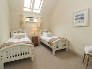 A bedroom with two single beds, a nightstand with a lamp, a window with curtains, and a framed picture on the wall. - Riverbank Cottage (Killin)