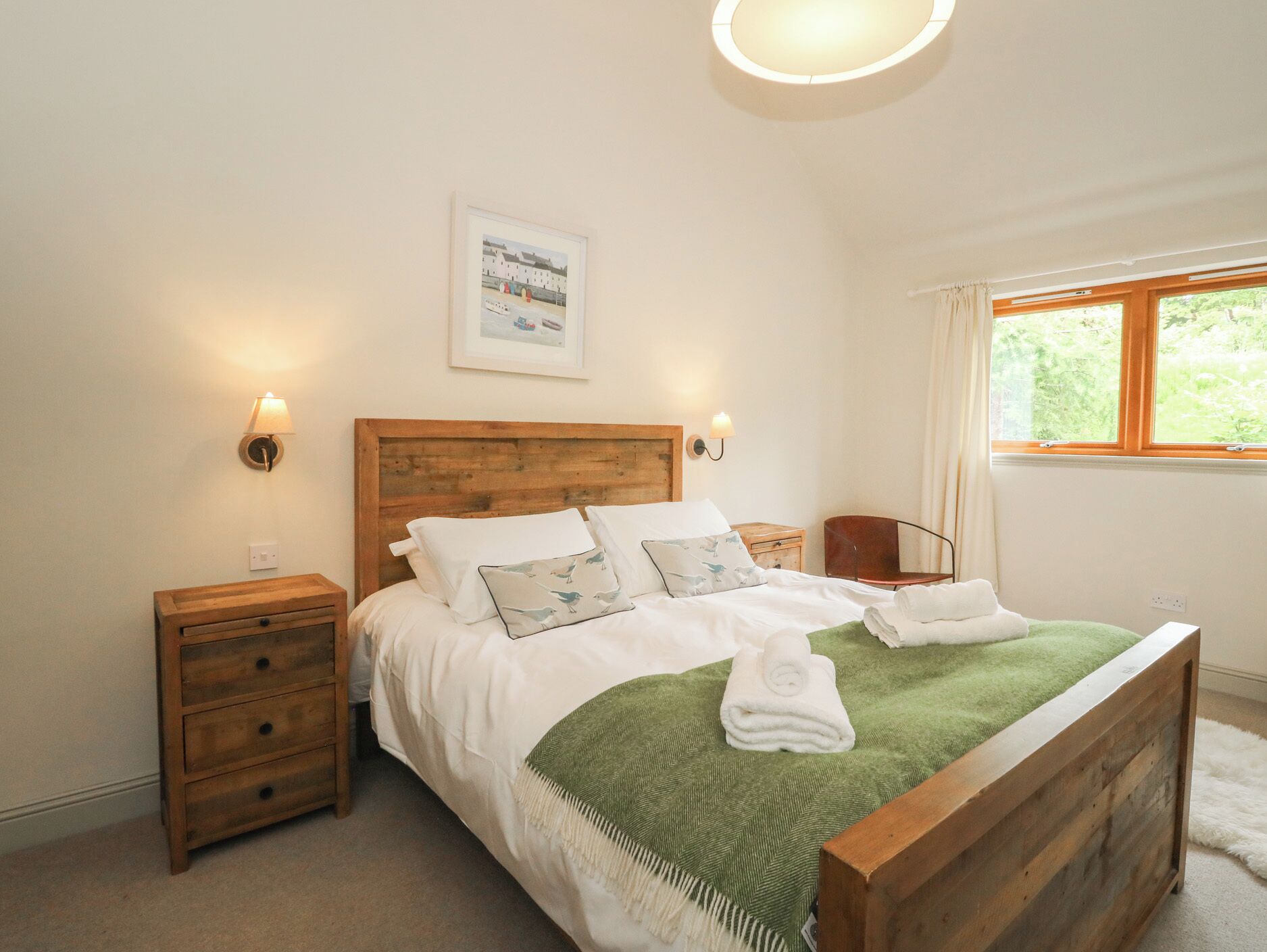 A bedroom with a wooden bed, two bedside tables, a green throw blanket, and a window with curtains.