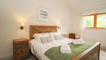A bedroom with a wooden bed, two bedside tables, a green throw blanket, and a window with curtains.