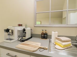 A kitchen with a coffee maker, a cutting board, and stacked towels.