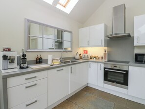 A modern kitchen with white cabinets, a built-in oven, a coffee machine, and a window above the sink. - Riverbank Cottage (Killin)