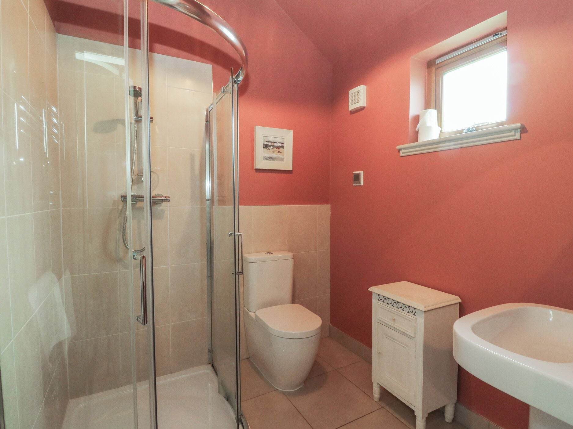 A bathroom with a glass-enclosed shower, a toilet, a sink, and a window.