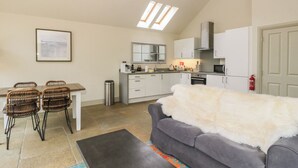 Ett kompakt bostadsutrymme med ett litet kök, en matplats och en grå soffa med en vit fäll.