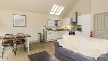 Un espacio habitable compacto con kitchenette, comedor y un sofá gris con un plaid de piel blanca.