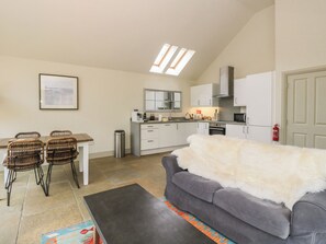 A compact living space with a kitchenette, dining area, and a gray sofa with a white fur throw. - Riverbank Cottage (Killin)