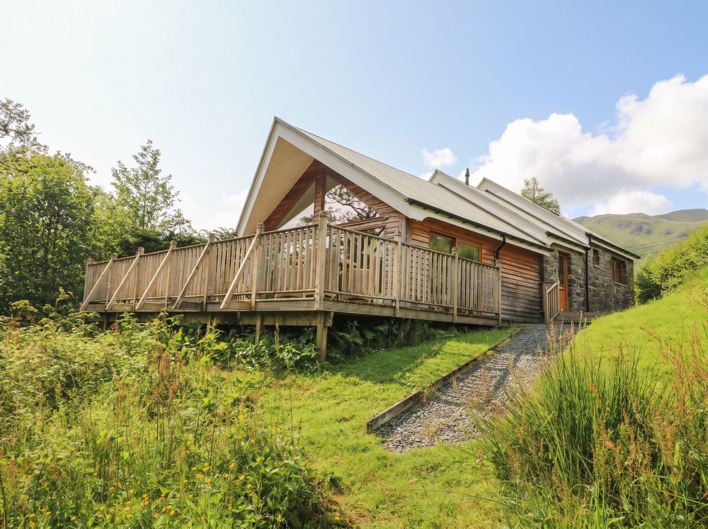 A wooden cabin with a sloped roof, a wooden deck, and a stone foundation.