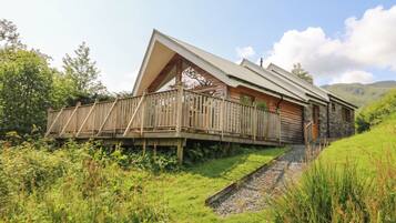 A wooden cabin with a sloped roof, a wooden deck, and a stone foundation.