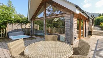 A wooden cabin with a glass-enclosed patio, a hot tub, and wicker furniture.