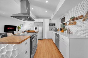 A modern kitchen with a central island, stainless steel appliances, and a flat-screen TV. - Villa Maris, Modern 5BR Getaway Near Miami Beach (North Miami)