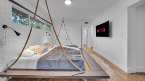 Une chambre moderne avec un lit suspendu, un téléviseur et un mur en briques blanches.