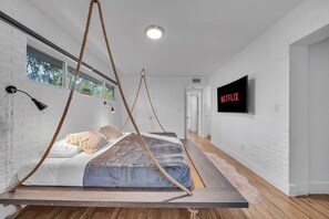A modern bedroom with a suspended bed, a television, and a white brick wall. - Villa Maris, Modern 5BR Getaway Near Miami Beach (North Miami)