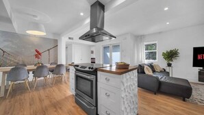 Une cuisine moderne avec un îlot central, un coin repas avec des chaises, un canapé et un téléviseur.