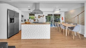 Une cuisine moderne dotée d’un îlot central, d’un coin repas avec une table et des chaises en bois, et offrant une vue sur l’extérieur.