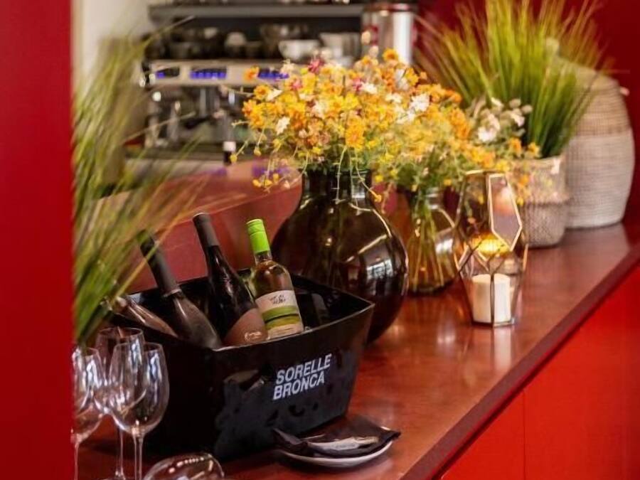 Eine Bar mit rotem Hintergrund, einem Flaschenhalter mit der Aufschrift 'Sorelle Bronca' und einer Vase mit gelben Blumen.