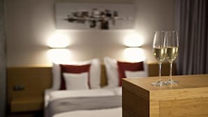 A hotel room with a bed, bedside lamps, and two glasses of white wine on a wooden table. - Wellness Hotel Abácie Nový Jičín (Novy Jicin)